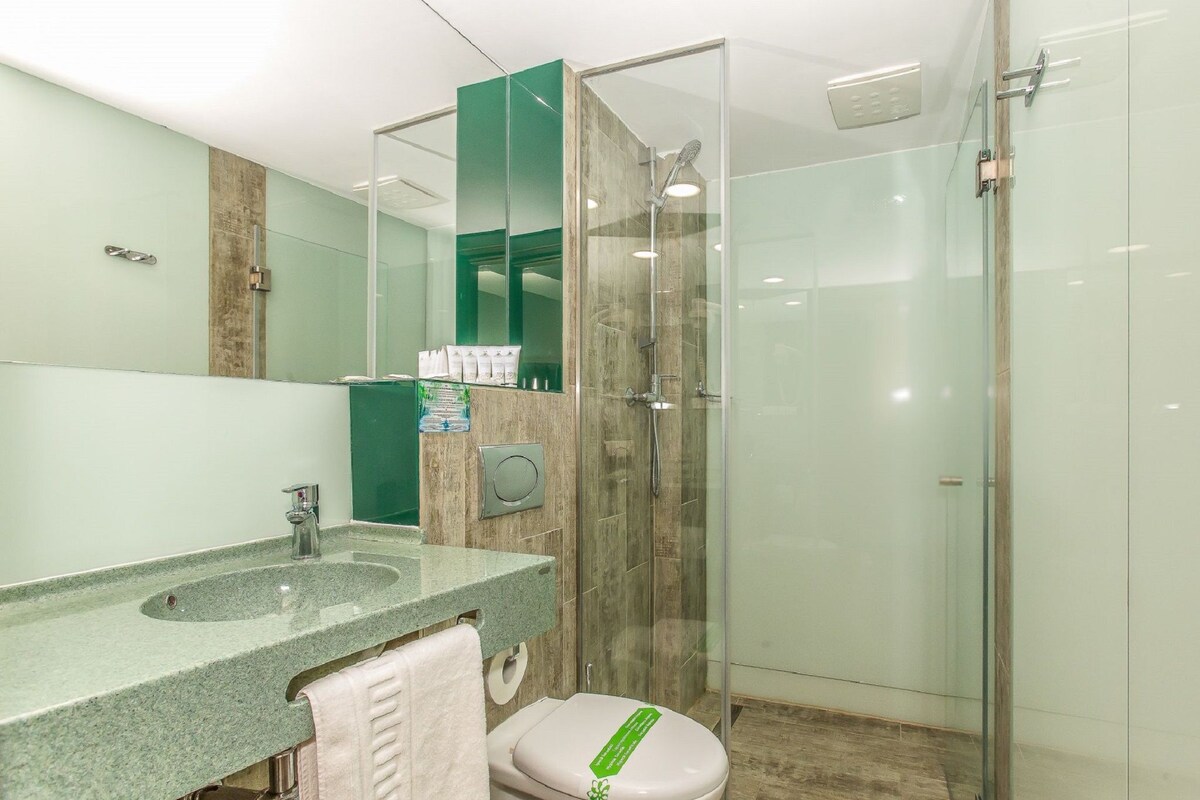 A modern bathroom with a granite sink, a glass shower enclosure, and a toilet with a green sign.