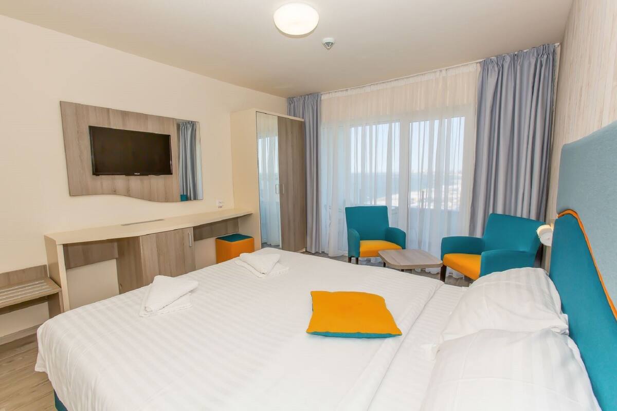 Ett hotellrum med en säng, en tv som är monterad på väggen, ett skrivbord och två stolar.
