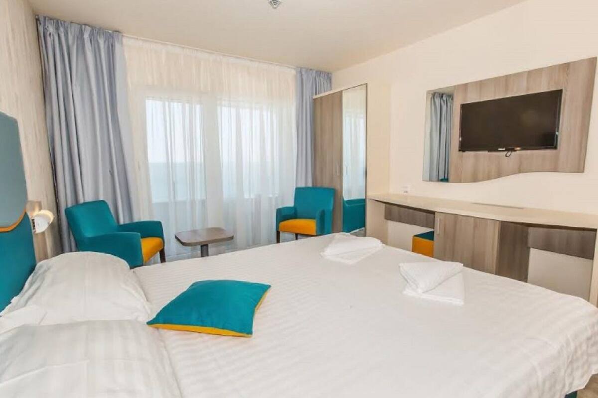 Ett hotellrum med en säng, två stolar, ett litet bord, en tv och en spegel.