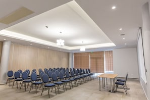 Ein Konferenzraum mit Reihen von Stühlen, einem Tisch und einem großen Fenster mit Vorhängen.