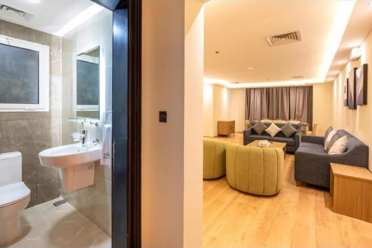 Un baño moderno con lavamanos y espejo, y una sala de estar con sofá y reposapiés.