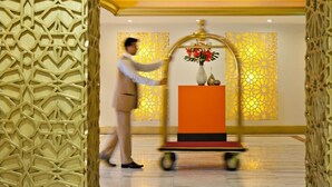 A man pushing a cart with a vase of flowers and a bottle, in a room with geometric patterned walls and a yellow ceiling. - Saray Mushereib Hotel (Doha)