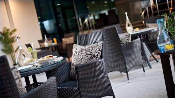 Outdoor wicker furniture with cushions, a glass table with plates and cutlery, and a decorative vase. - Saray Mushereib Hotel (Doha)
