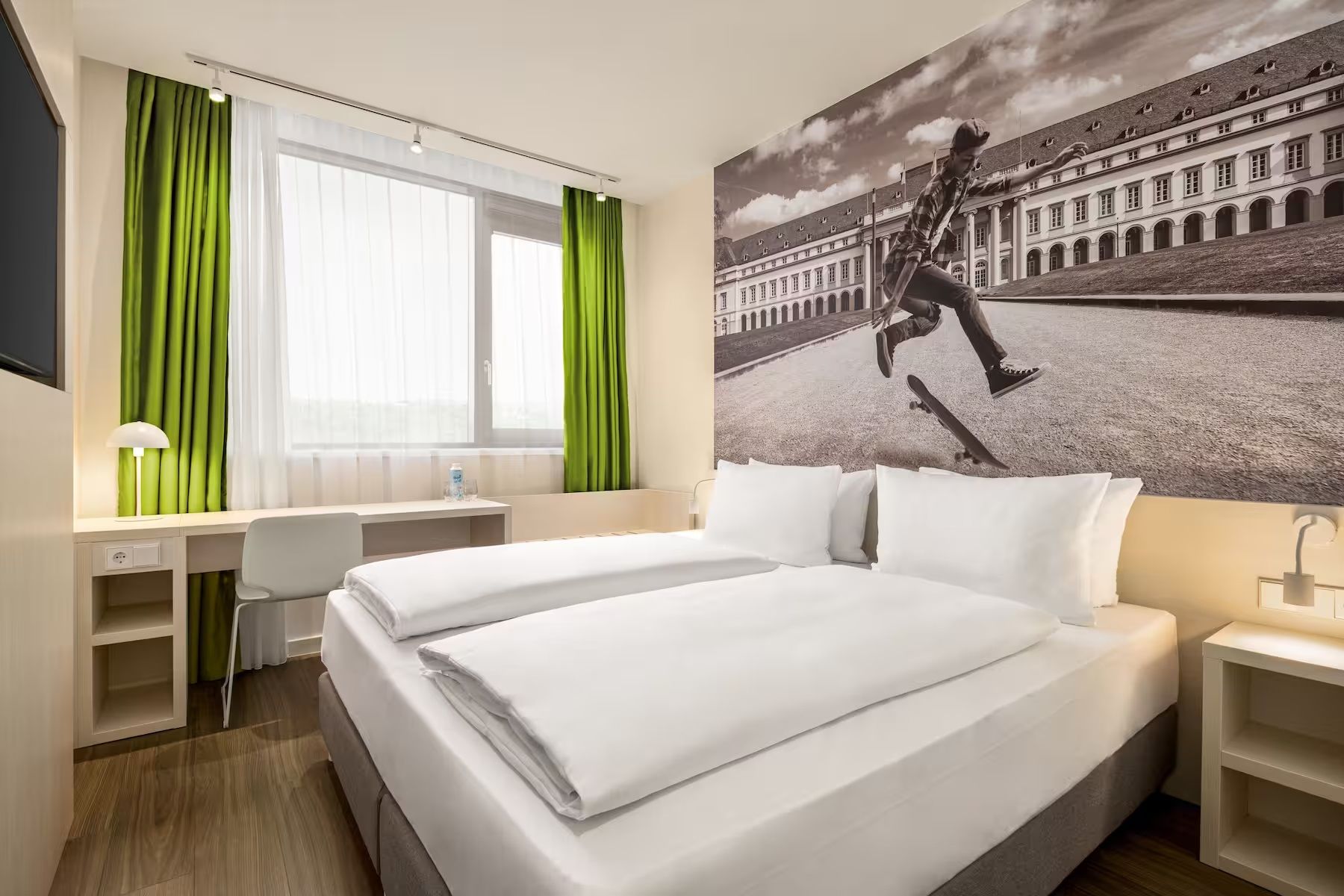 Ein Hotelzimmer mit Bett, Schreibtisch, Stuhl und einem großen Fenster mit Vorhängen.