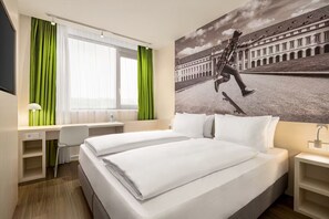 Una habitación de hotel con cama, escritorio, silla y un ventanal con cortinas.