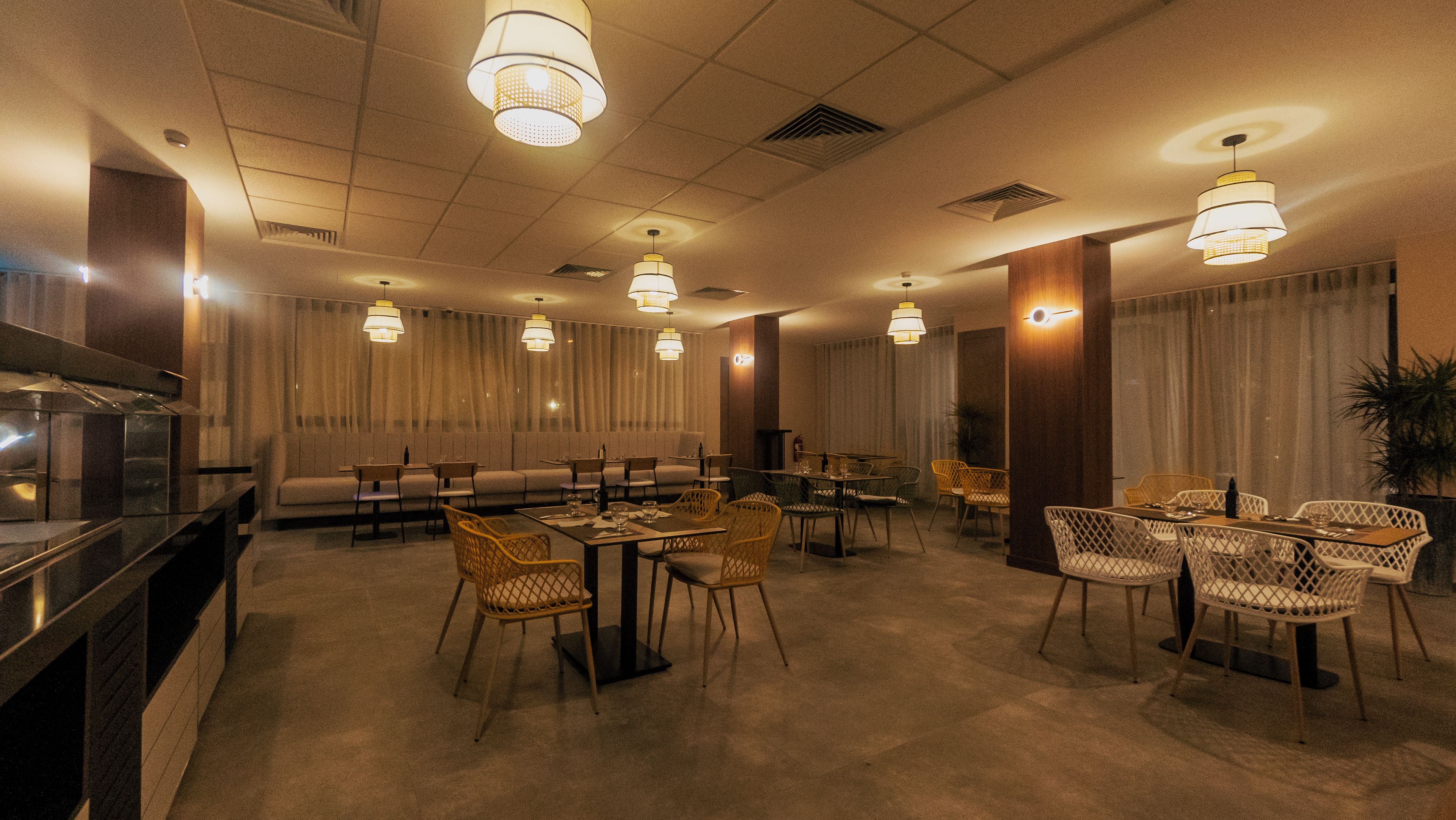 Uma área de refeições de hotel com várias mesas e cadeiras, um sofá e uma cozinha.