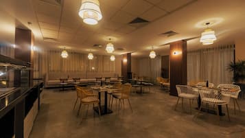Uma área de refeições de hotel com várias mesas e cadeiras, um sofá e uma cozinha.