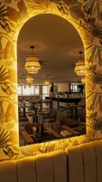 A restaurant with a central seating area, multiple hanging lights, and a visible kitchen in the background.