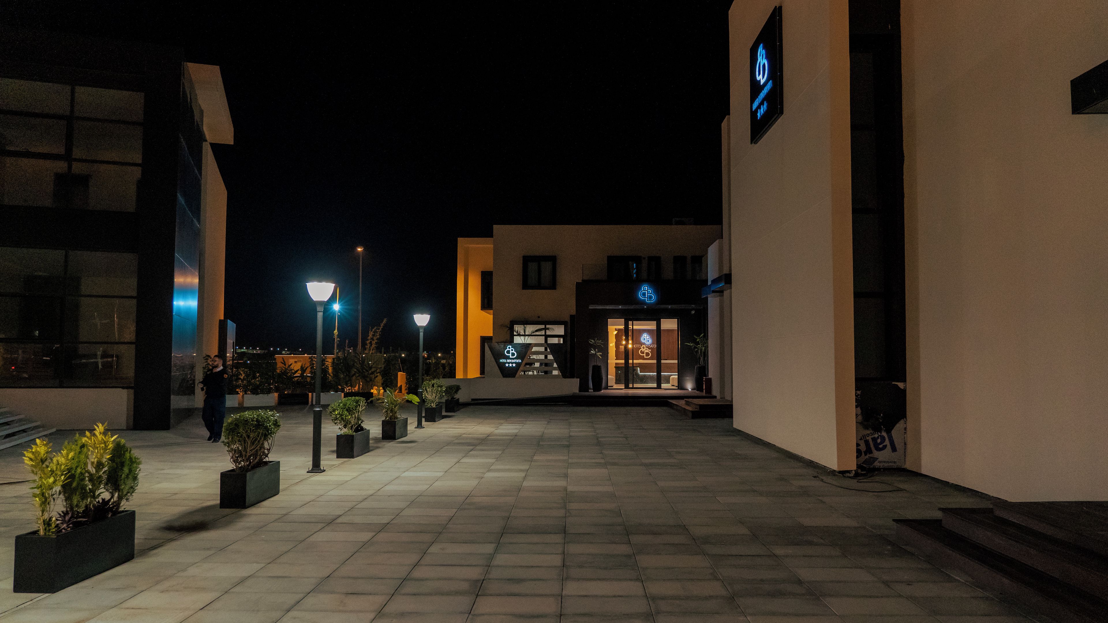A nighttime view of a building with a reception area, outdoor lighting, and potted plants.