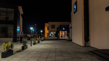 A nighttime view of a building with a reception area, outdoor lighting, and potted plants.