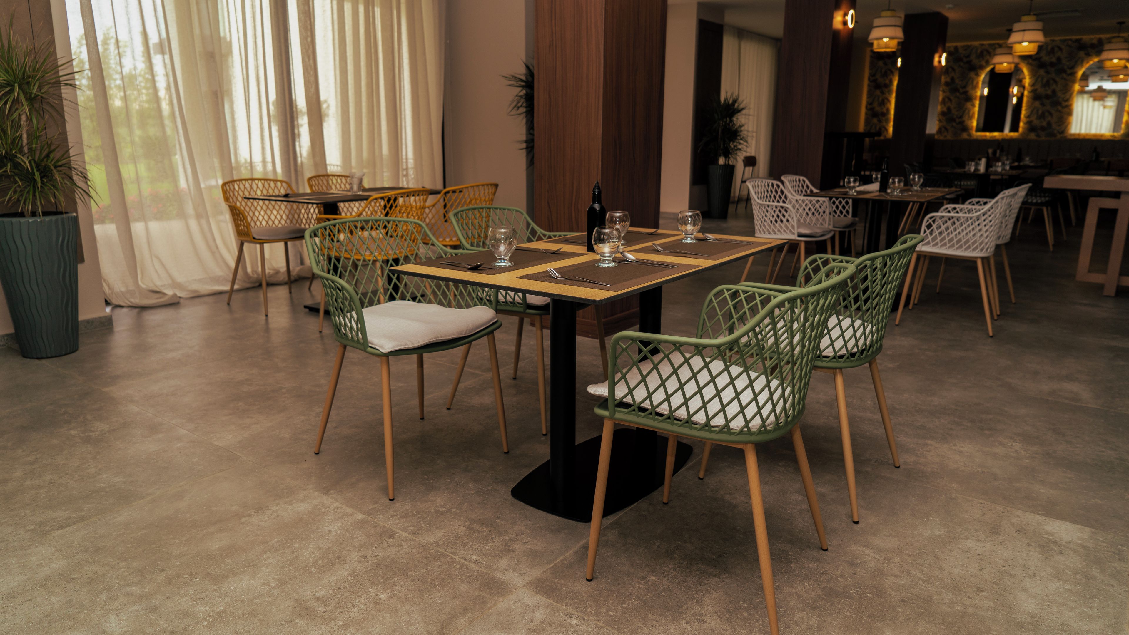 A dining area with green chairs, a wooden table, and a potted plant.