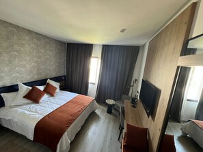 Quarto de hotel com uma cama, televisão, mesa pequena e uma cadeira.