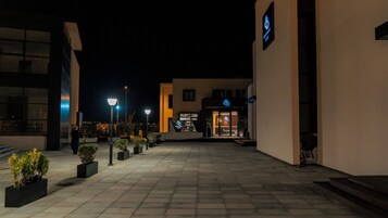 A nighttime view of a building with a reception area, outdoor lighting, and potted plants.