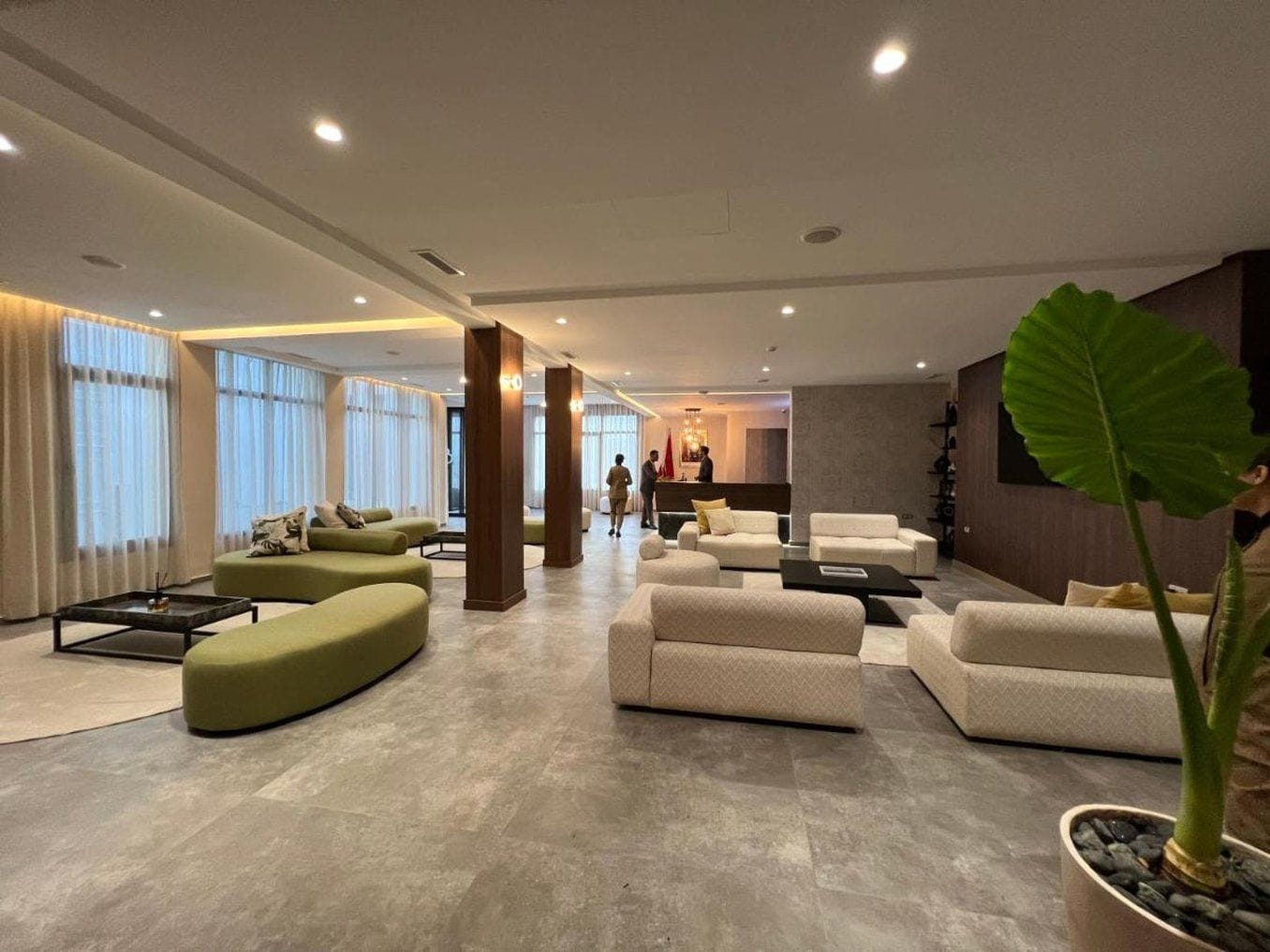 Eine großzügige Hotelhalle mit einer Rezeption, Sitzgeboten und einer großen Pflanze.