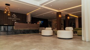 Et hotellets reception område med en marmor bordplade, en moderne lysekrone og et siddeområde med polstrede stole.