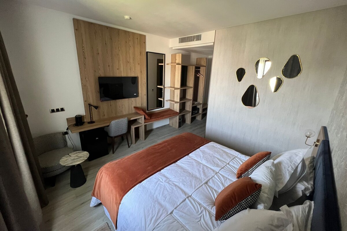 Et moderne hotelværelse med en stor seng, et skrivebord, et fjernsyn og et skab.