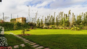 Un área verde con un sendero de piedra que lleva a un edificio, rodeado de plantas y árboles.