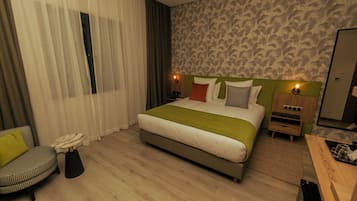 Quarto de hotel com cama, cadeira, mesa de cabeceira e criado-mudo.