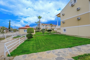 A courtyard with a stone pathway, a white railing, and a building with multiple windows and air conditioning units. - Goldlion Hotel (Fethiye)