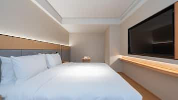Una habitación de hotel con una cama grande, un televisor montado en la pared y una mesita de noche pequeña.