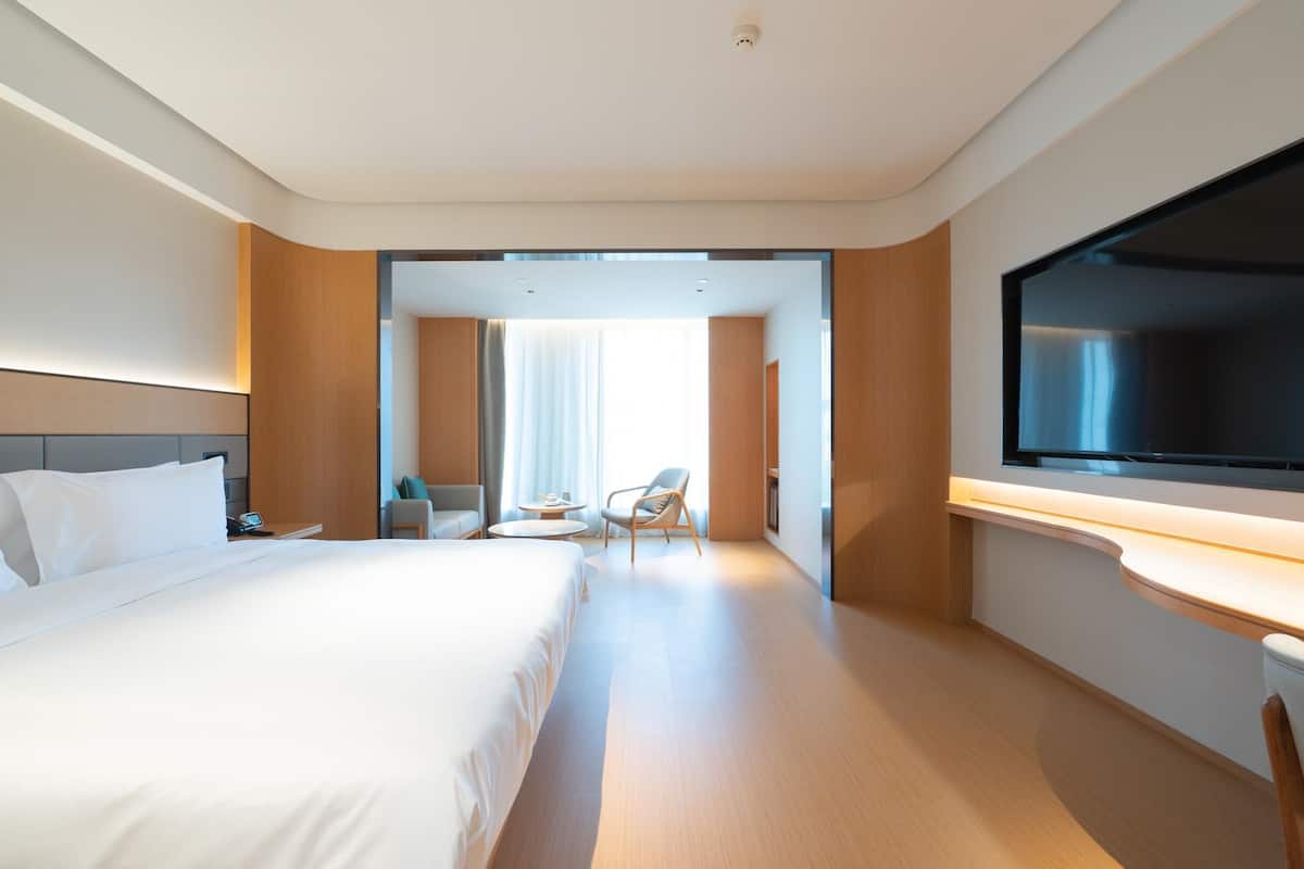 Quarto de hotel com uma cama grande, televisão presa à parede, escrivaninha e uma cadeira.