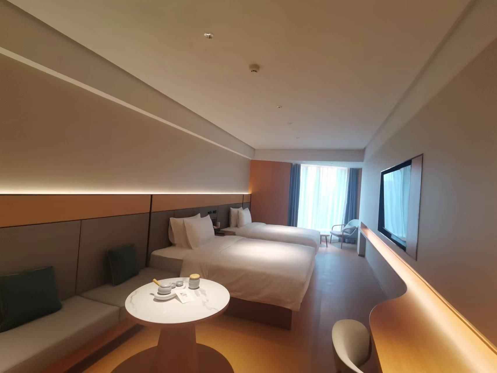A modern hotel room with a large bed, a sofa, a small table, and a TV.