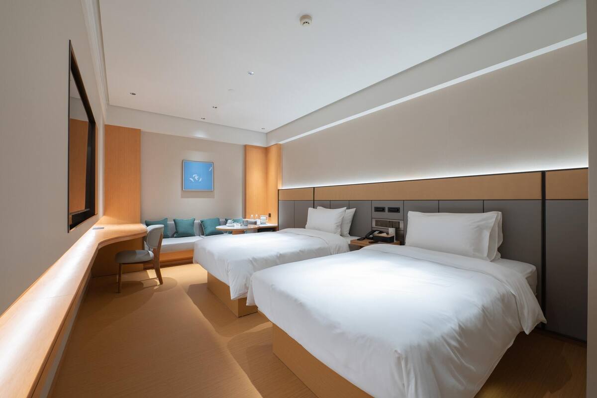 Quarto de hotel com duas camas, uma escrivaninha, uma cadeira e uma mesinha.