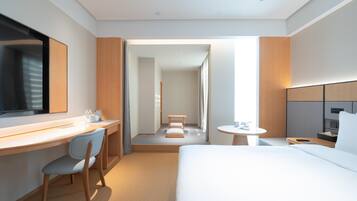 A modern hotel room with a bed, desk, chair, and a small table.
