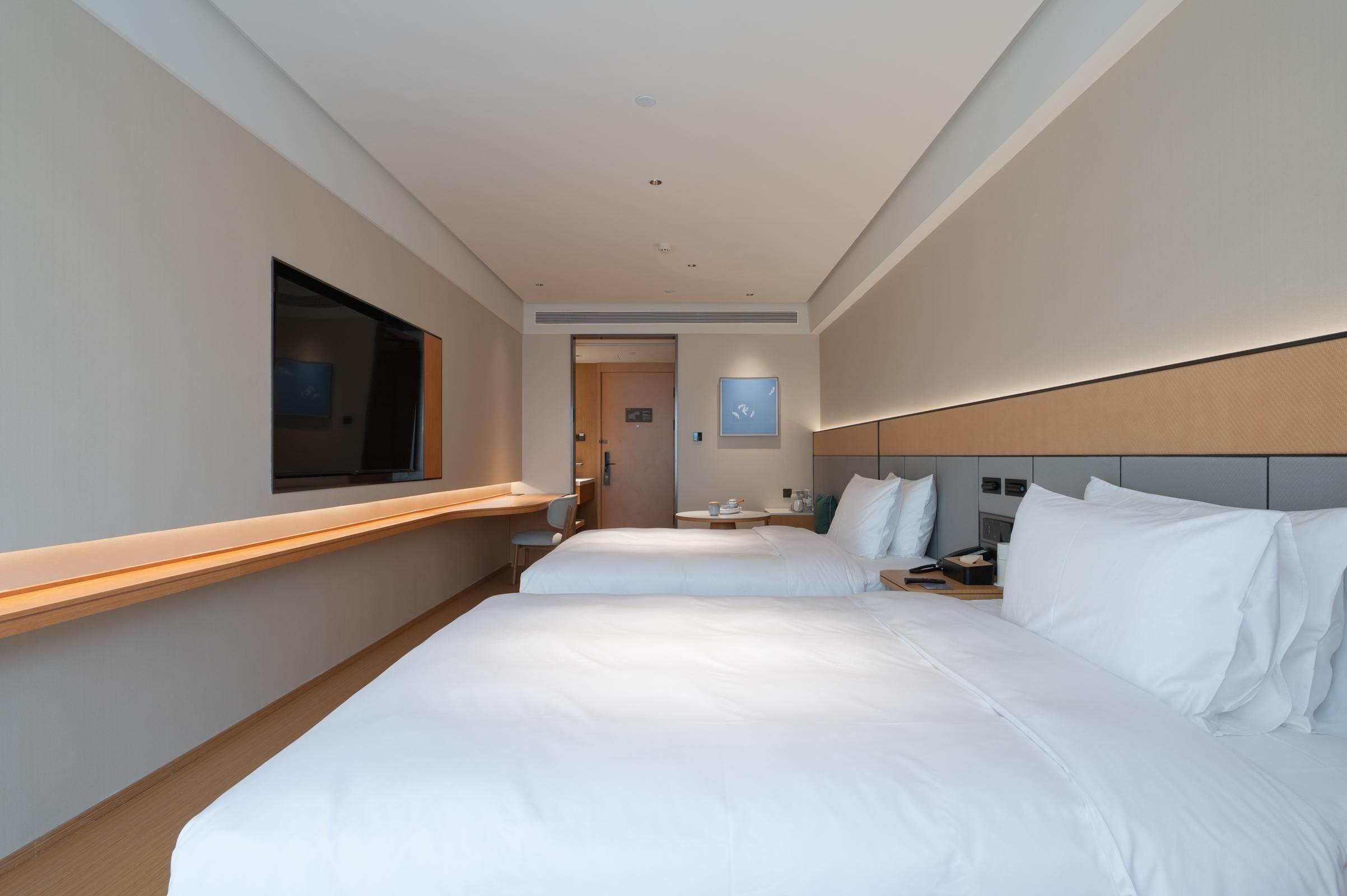 Habitación de hotel con dos camas, un escritorio, una silla, un televisor y una mesita de noche.