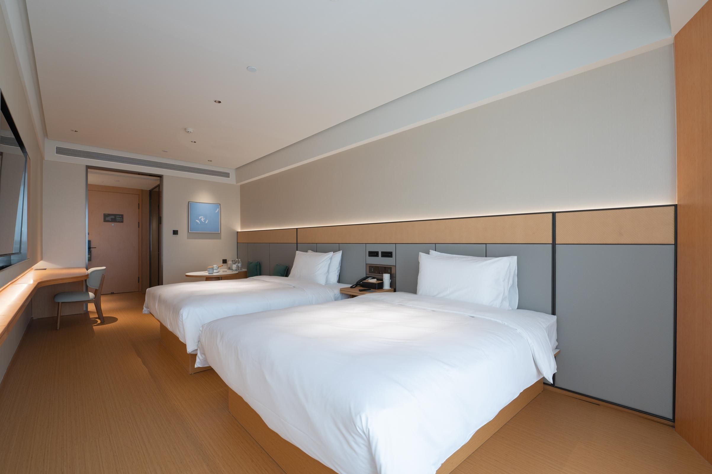 A hotel room with two beds, a desk, a chair, and a small table with a phone.
