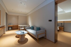 Ett modernt hotellrum med en soffa, ett runt soffbord, ett skrivbord och ett litet pentry.