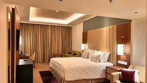 Quarto de hotel moderno com uma cama grande, uma escrivaninha, um sofá e uma televisão.