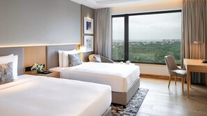 Quarto de hotel com duas camas, uma escrivaninha e uma janela grande com vista para a cidade.