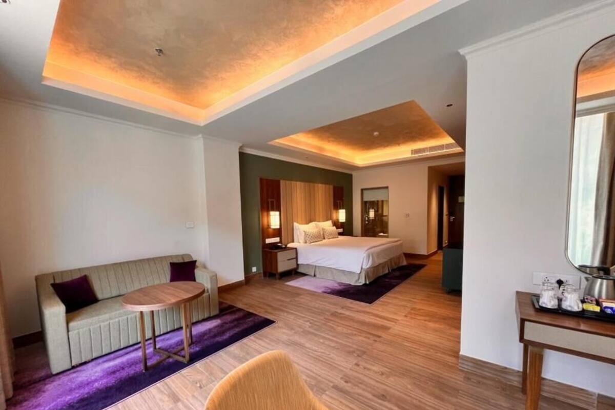 Ein Hotelzimmer mit einem Bett, einem Sofa, einem kleinen runden Tisch, einem Sessel, einem Spiegel und Holzboden.