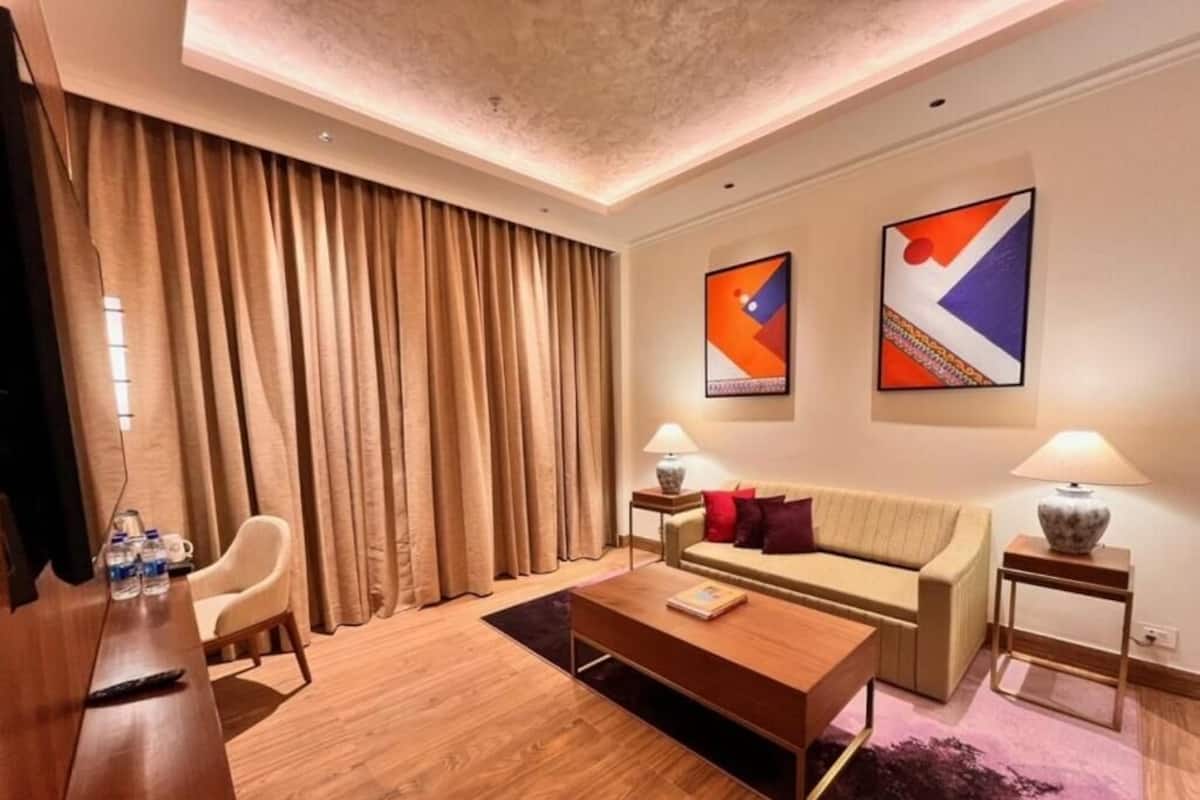 A modern hotel room with a wooden coffee table, a sofa, a TV, and a large window with curtains.