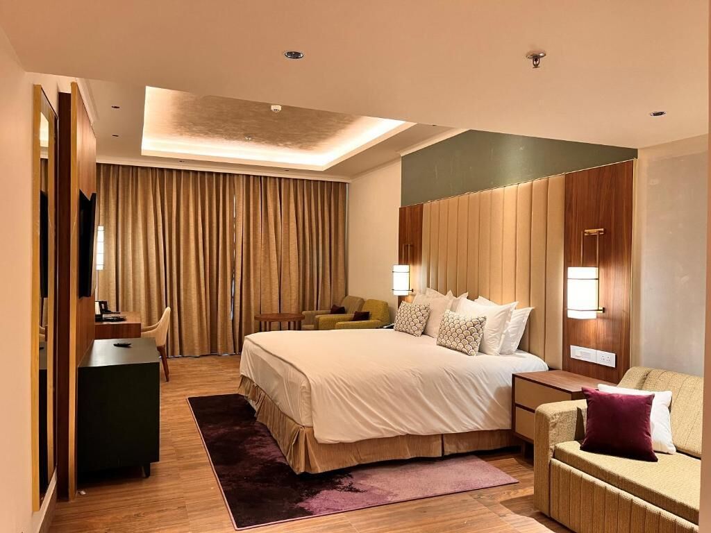 A modern hotel room with a large bed, a desk, a sofa, and a TV.