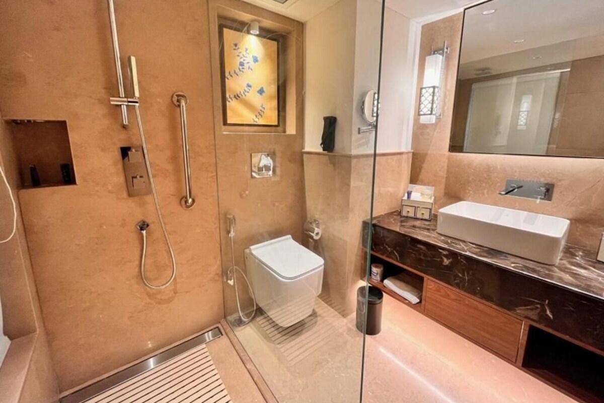Een moderne badkamer met een douchecabine van glas, een witte wastafel en een marmeren aanrecht.