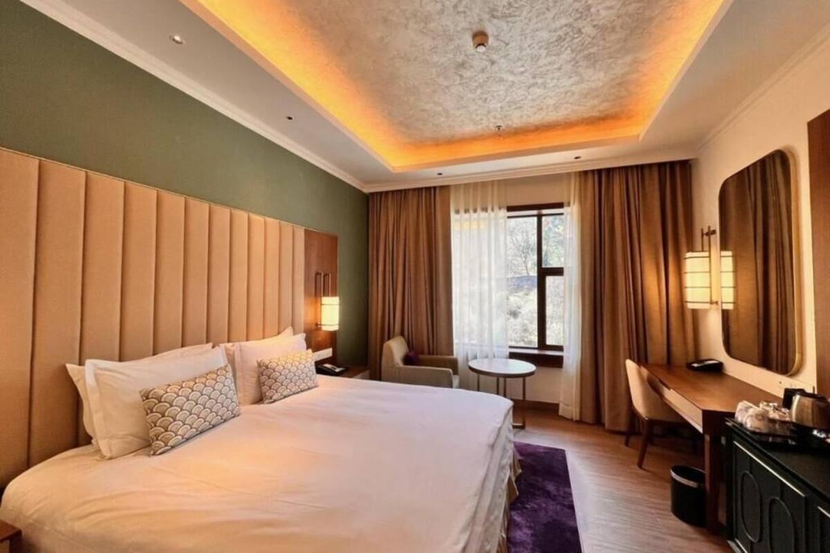 Ein Hotelzimmer mit einem großen Bett, einem Schreibtisch, einem Stuhl, einem kleinen Tisch und einem Fenster mit Vorhängen.