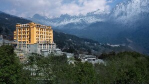 A multi-story hotel with a yellow facade, set against a backdrop of snow-capped mountains and a clear sky. - Vivanta Tawang Arunachal Pradesh (Tawang)