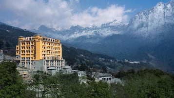 A multi-story hotel with a yellow facade, set against a backdrop of snow-capped mountains and a clear sky.