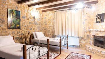 A room with stone walls, a fireplace, two beds, and a painting.