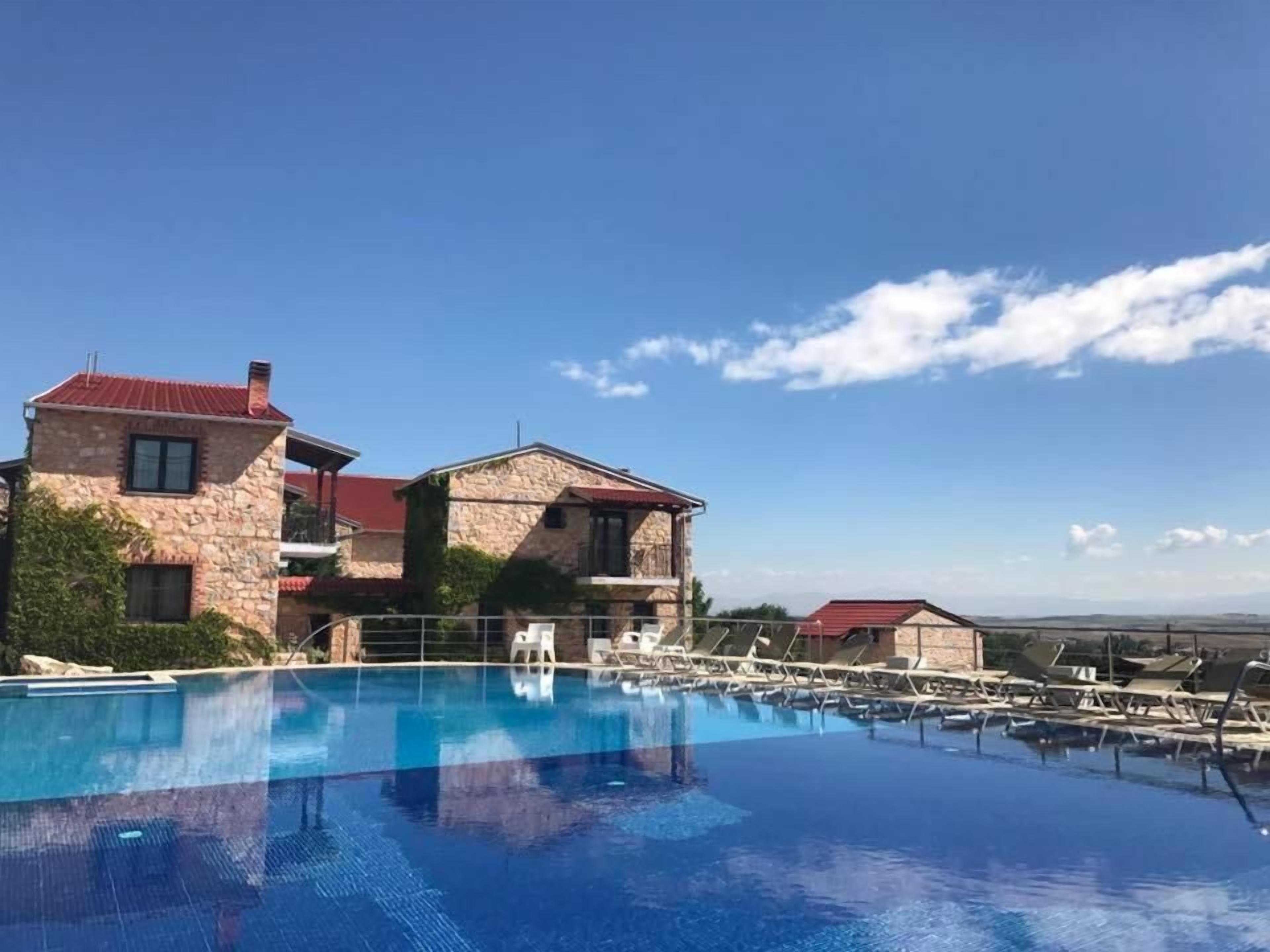 A pool area with a stone building, lounge chairs, and a clear blue sky.