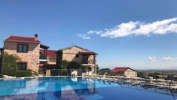 A pool area with a stone building, lounge chairs, and a clear blue sky.