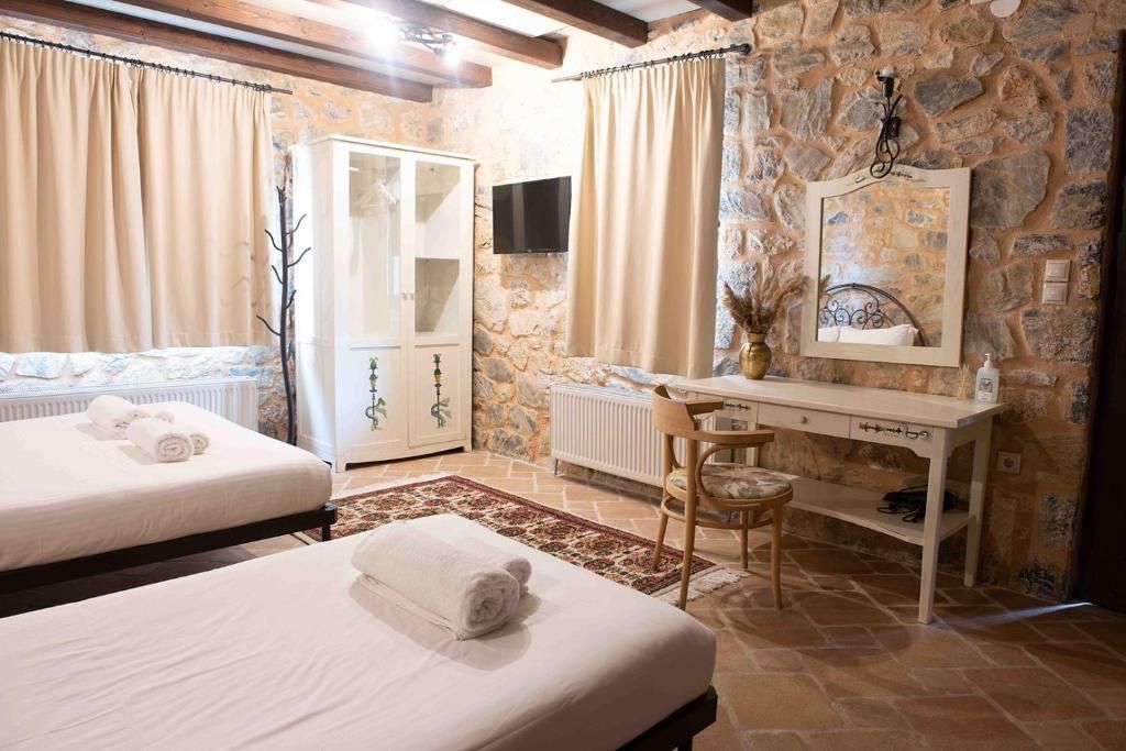 A bedroom with two beds, a desk, a chair, a radiator, and a stone wall.