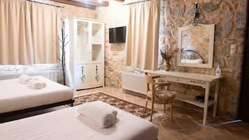 A bedroom with two beds, a desk, a chair, a radiator, and a stone wall.