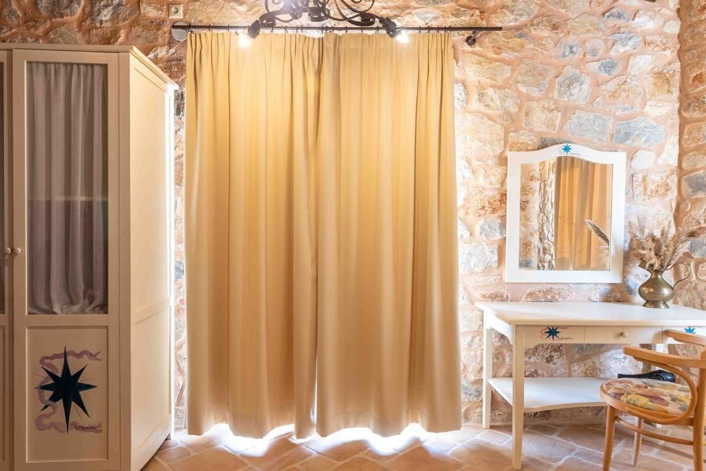 Ein Zimmer mit Stehwänden, einem Holzkasten mit Sternenmuster, einem gelben Vorhang, einem Holztisch und einem Stuhl.