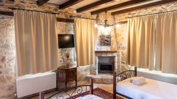 A cozy room with stone walls, a fireplace, two beds, and a TV.