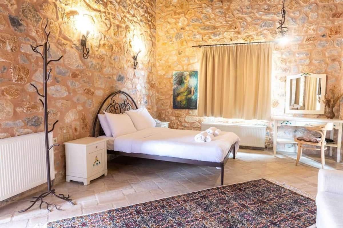 A bedroom with a stone wall, a bed, a nightstand, a dresser, and a window with curtains.