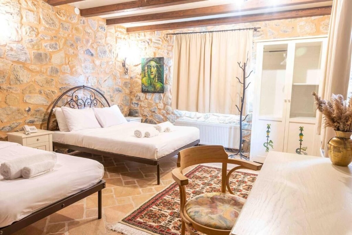 Un dormitorio con dos camas, una pared de piedra, un cuadro y vistas al exterior.