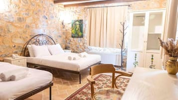 A bedroom with two beds, a stone wall, a painting, and a view of the outside.